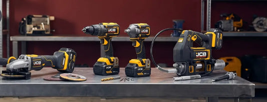 Zestaw akumulatorowych narzędzi JCB na stole warsztatowym, wiertarka, zakrętarka, szlifierka i smarownica