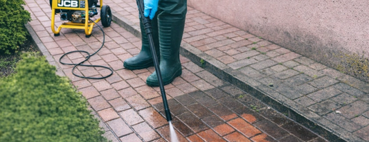 Mycie kostki brukowej strumieniem wody z lancy w w tle myjka JCB z przewodem