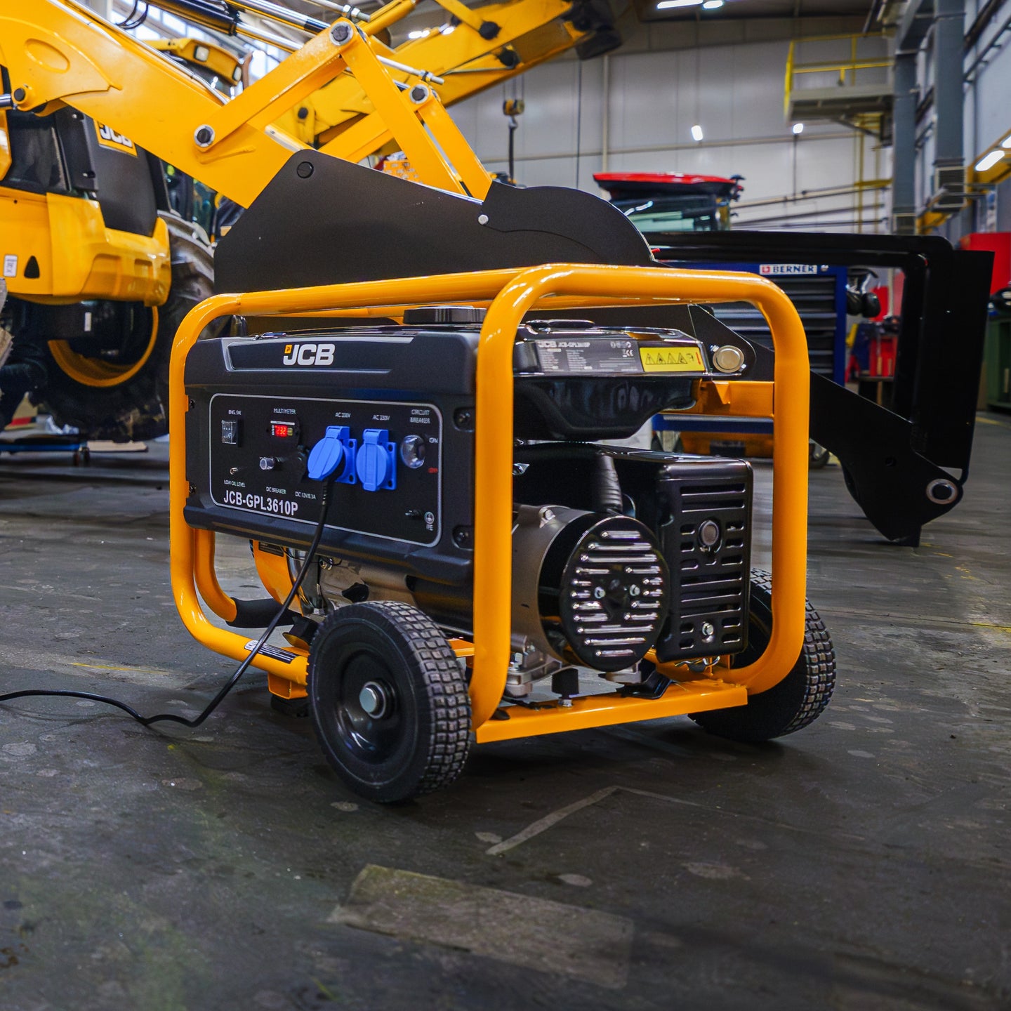 Mały agregat prądotwórczy JCB GPL3610P 3,6 kW podłączony w hali serwisowej na tle maszyn budowlanych JCB