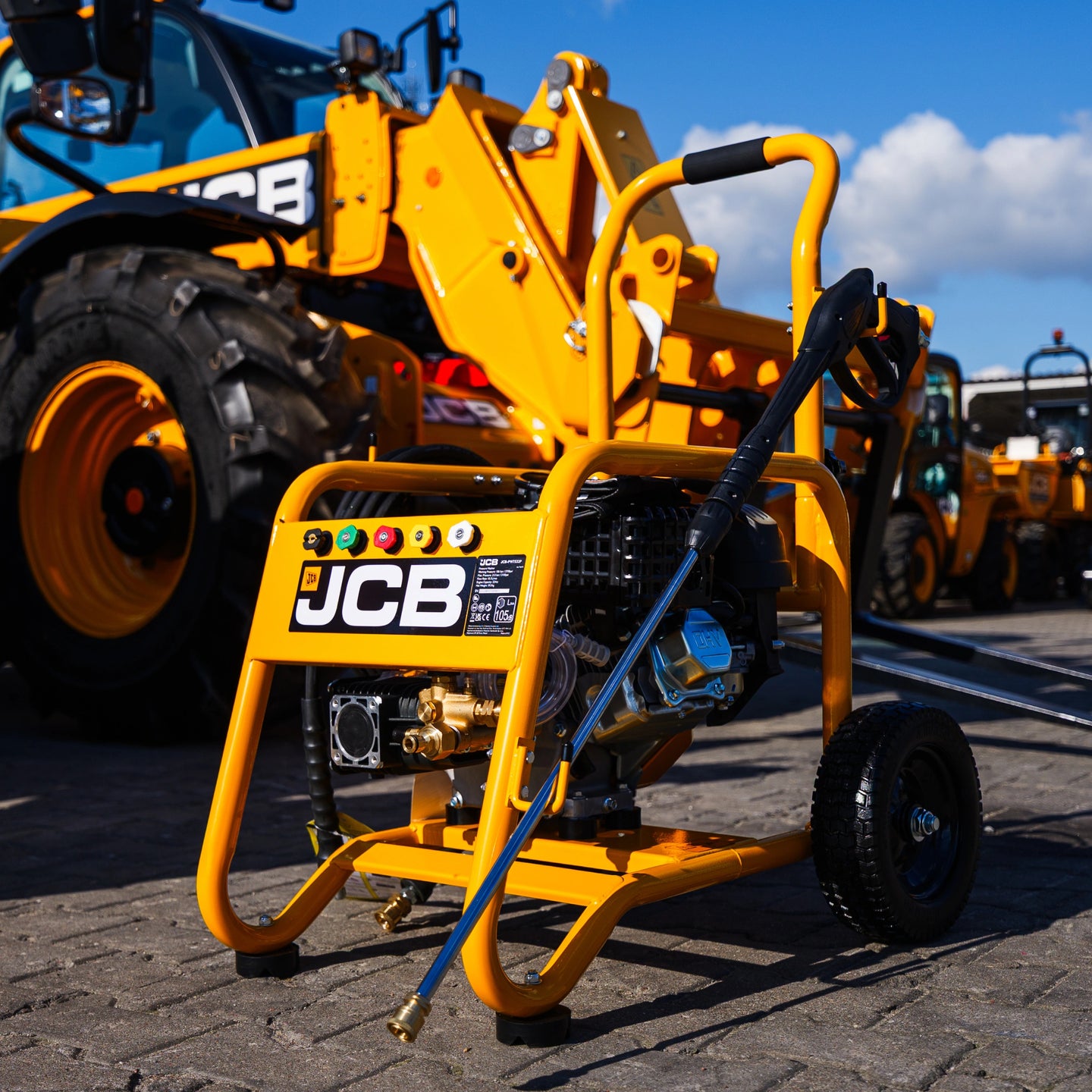 Myjka ciśnieniowa JCB PW15040PP24 ujęcie z przodu lanca oparta o żółtą ramę pompa annovi reverberi koła terenowe w tle maszyny JCB na placu