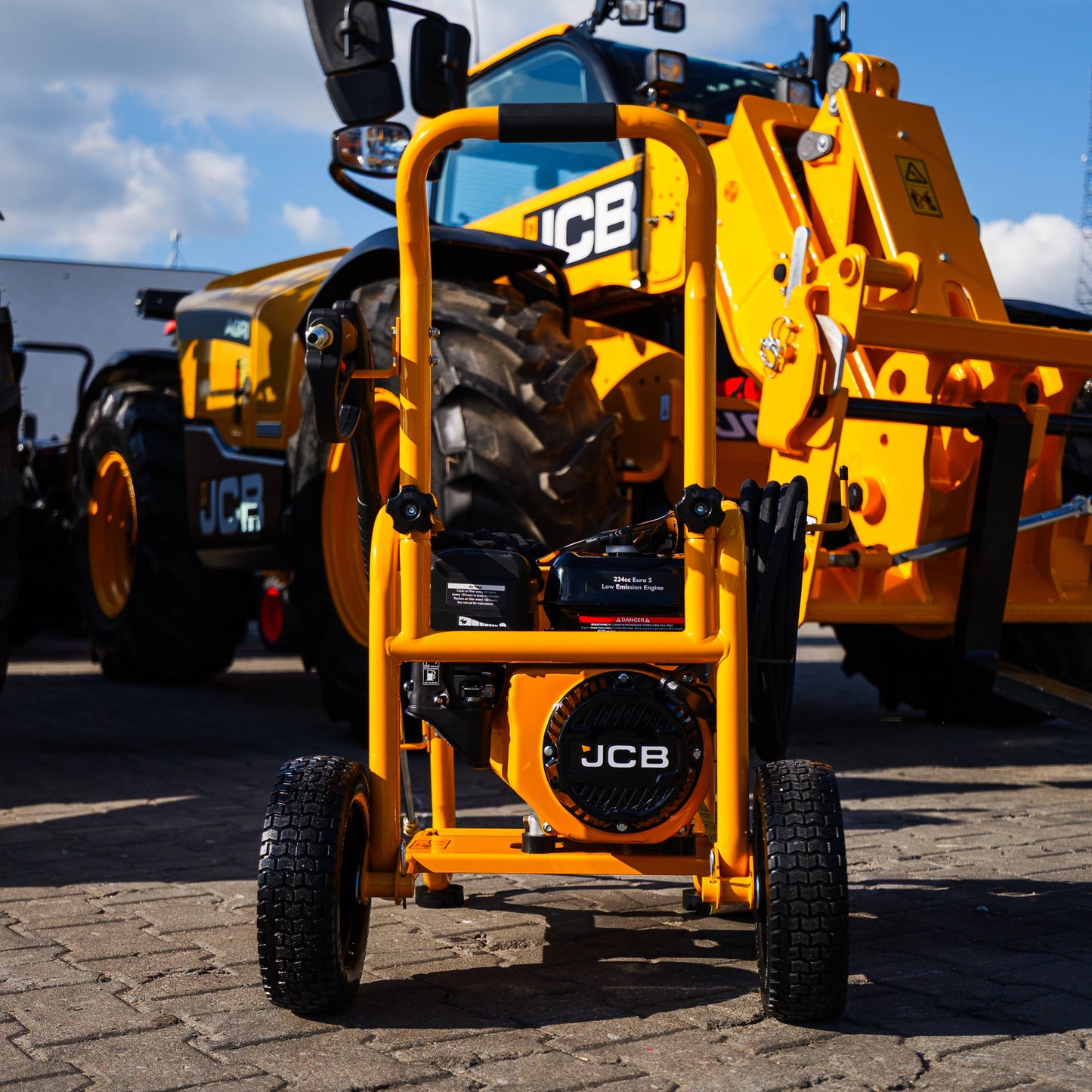 Myjka ciśnieniowa JCB PW7532P24 tył czarne koła terenowe żółta rama widoczny silnik JCB z przewodem wysokociśnieniowym w tle maszyny JCB
