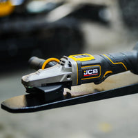 szlifierka kątowa JCB Professional 18V z płaską głowicą podczas szlifowania metalu z iskrami trzymana oburącz z tekstem Płaska głowica