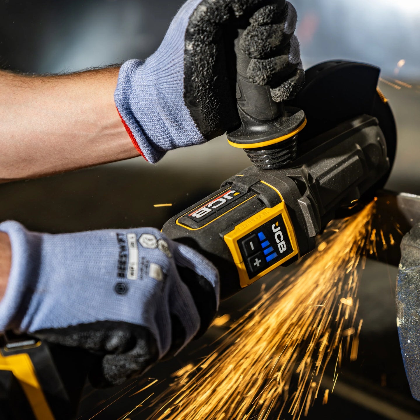 szlifierka kątowa JCB Professional 18V z płaską głowicą podczas szlifowania metalu w warsztacie z iskrami z tekstem Silnik bezszczotkowy