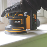 szlifierka mimośrodowa JCB Professional 18V podczas szlifowania drewna trzymana w rękawicy z tekstem Silnik bezszczotkowy