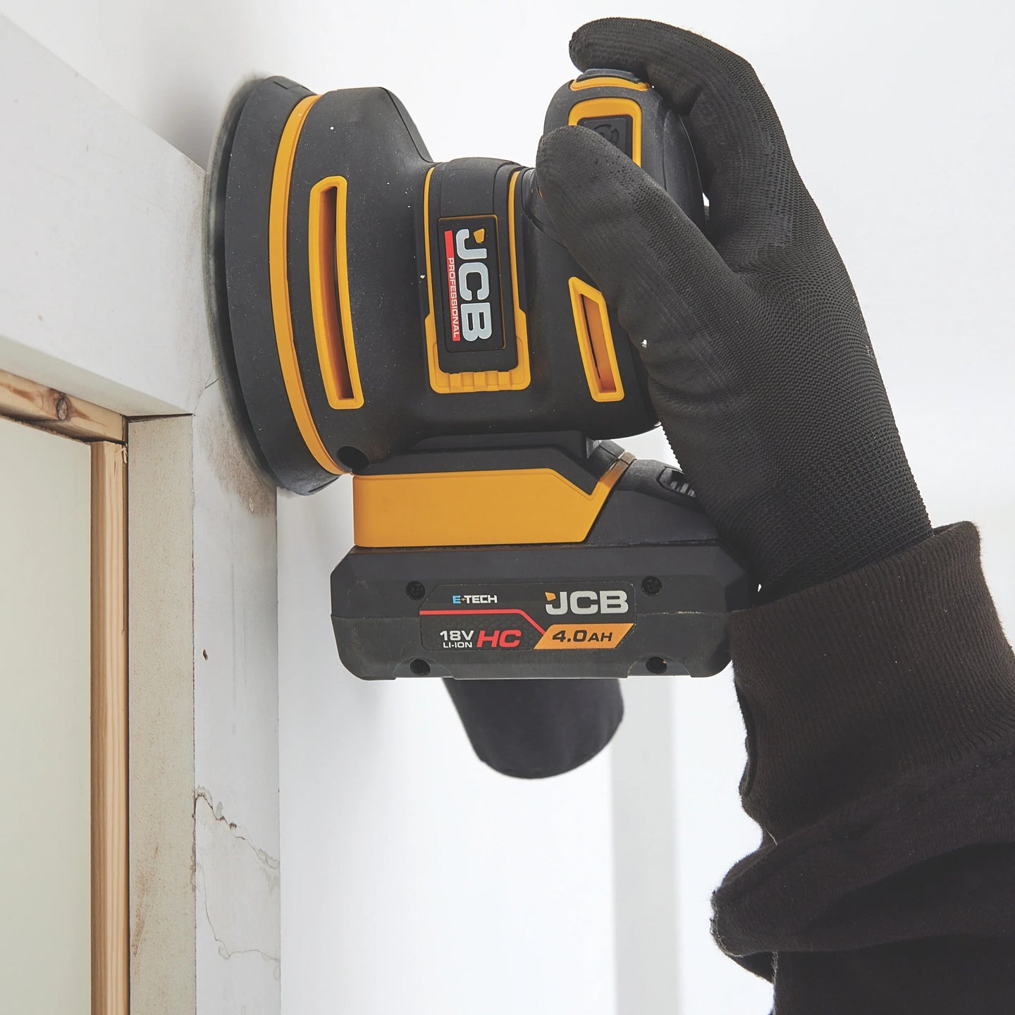 szlifierka mimośrodowa JCB Professional 18V z akumulatorem HC 4.0Ah podczas szlifowania parapetu ujęcie z bliska z tekstem Uniwersalna podkładka na rzep